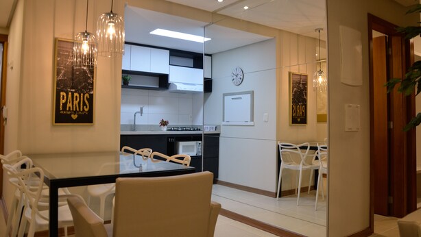 Una cocina moderna con armarios blancos, un microondas y un comedor con una mesa y sillas de vidrio.