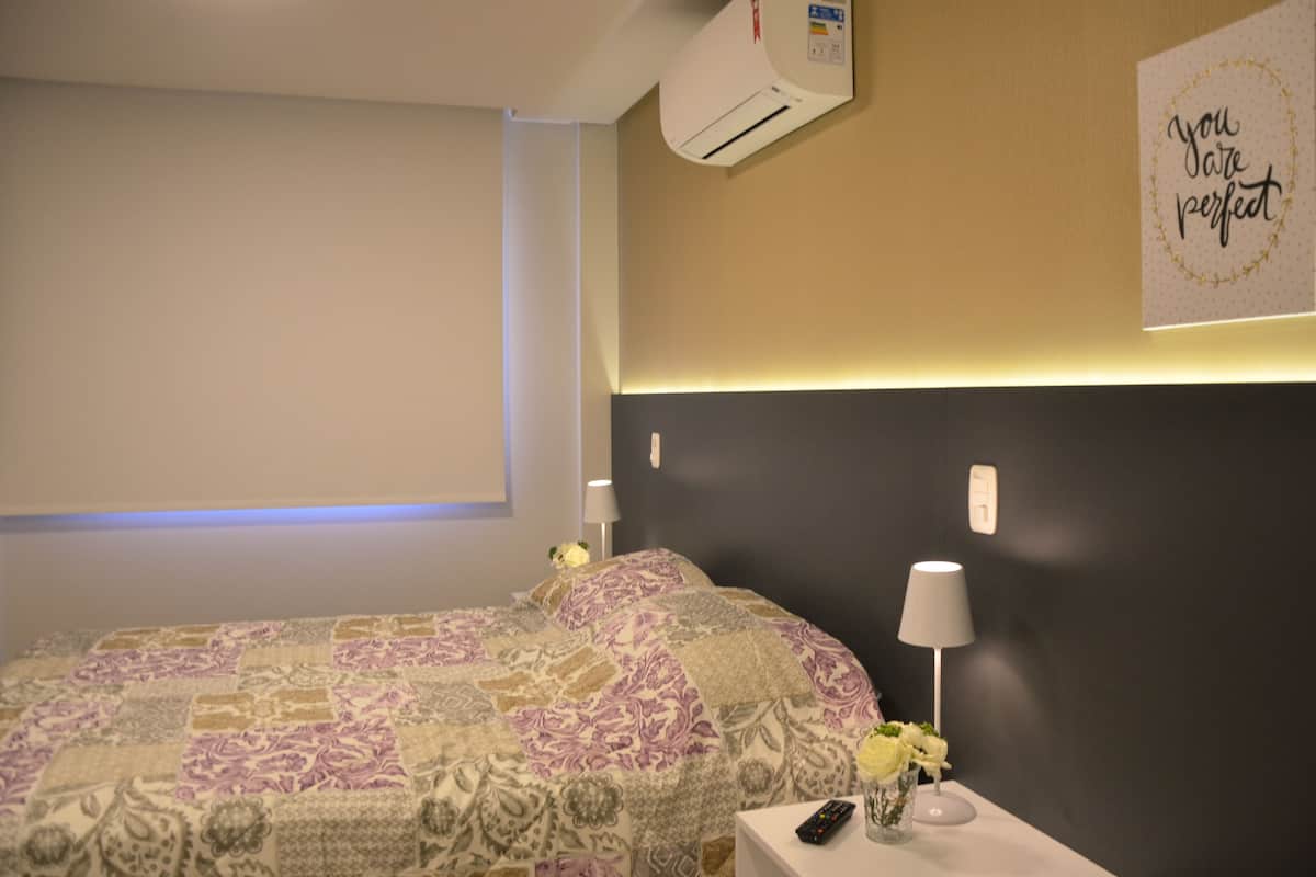 A hotel room with a bed, bedside lamps, a wall-mounted air conditioner, and a motivational poster.