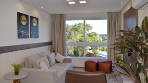 Una sala de estar moderna con un sofá, una mesa de centro y un ventanal que ofrece vistas a árboles y edificios.