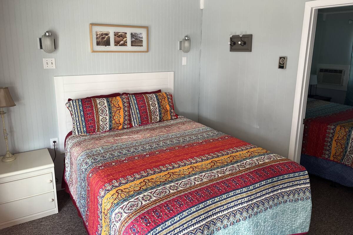 A bedroom with a large bed, a bedside table, a lamp, and a wall-mounted picture.