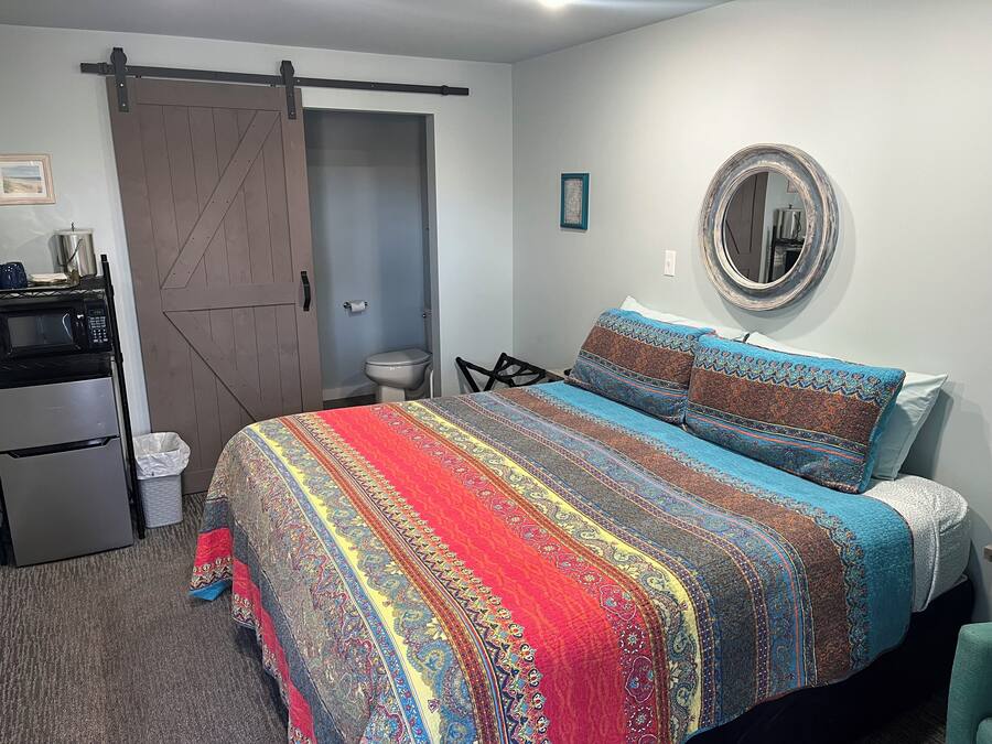 Un dormitorio con cama, cómoda, microondas, refrigerador, puerta corrediza, inodoro y espejo en la pared.
