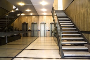 Un hall d’entrée moderne avec un sol en marbre, un escalier et trois ascenseurs.