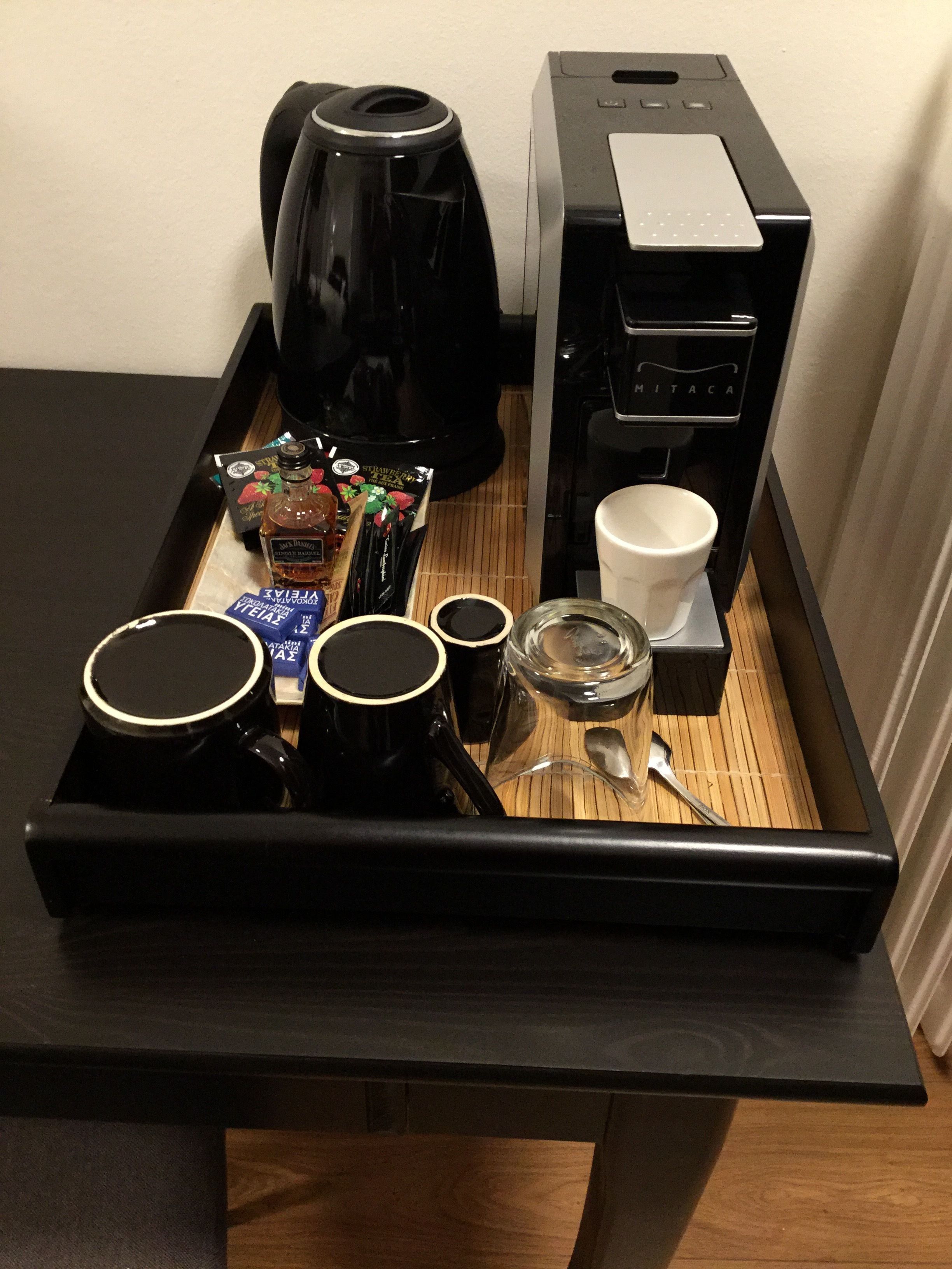 A tray with a coffee maker, a tea kettle, a coffee machine, cups, a glass, and a spoon.