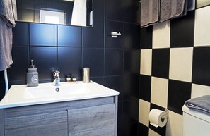 Casa de banho com lavatório branco, paredes em azulejo escuro e padrão xadrez preto e branco.