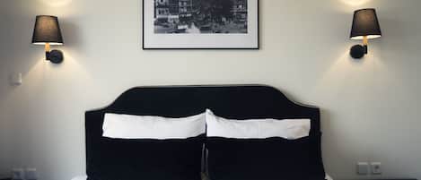 Ein ordentlich bezogenes Bett mit schwarz-weißer Bettwäsche, zwei Wandlampen und ein gerahmtes Stadtbild darüber.