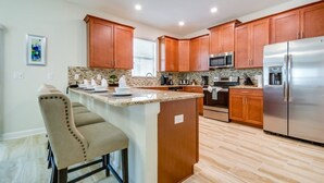 A modern kitchen with wooden cabinets, a stainless steel refrigerator, and a granite countertop. - 1538MVD (Davenport)