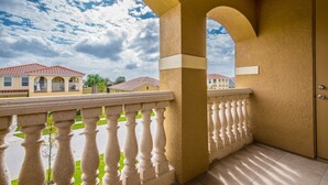 Un balcone con ringhiera bianca che si affaccia su una zona residenziale con case e un cielo nuvoloso.
