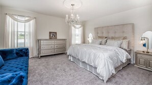 A bedroom with a large bed, a dresser, a blue armchair, and a chandelier. - 6 Bedroom King Castle Home (Kissimmee)
