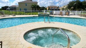 A swimming pool with a hot tub in the center, surrounded by lounge chairs and a fence. - 1509SD (Clermont)