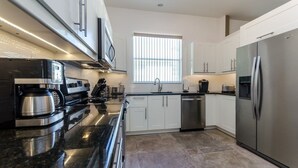 A modern kitchen with stainless steel appliances, white cabinetry, and a large window providing natural light. - North Hampton Pool House (Davenport)