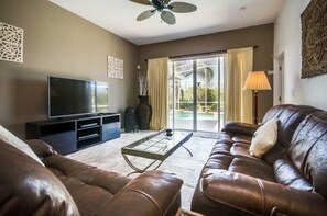 A living room with a leather sofa, a flat-screen TV, a coffee table, and a sliding glass door leading to a balcony. - North Hampton Pool House (Davenport)