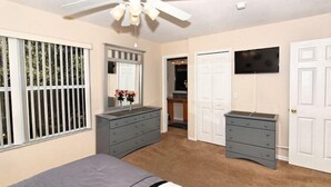 A bedroom with a bed, a dresser, a vanity, a ceiling fan, and a TV mounted on the wall. - 716TL (Davenport)