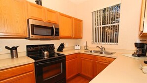 A modern kitchen with wooden cabinets, a stainless steel microwave, a black stove, and a window with bars. - 716TL (Davenport)