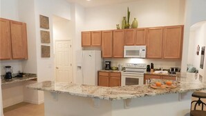 A kitchen with wooden cabinets, a microwave, a refrigerator, and a granite countertop. There are two stools and a small island with a sink. - Crane's Roost Villa (Davenport)