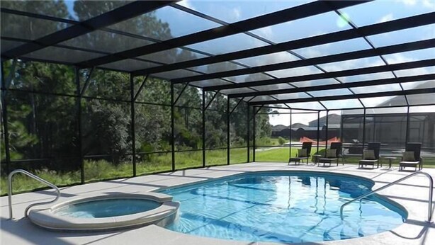 A covered swimming pool with a hot tub, surrounded by lounge chairs and a view of a grassy area with trees. - Crane's Roost Villa (Davenport)