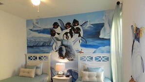 A bedroom with two single beds, a nightstand with a lamp, and a mural of penguins on the wall. - Crane's Roost Villa (Davenport)