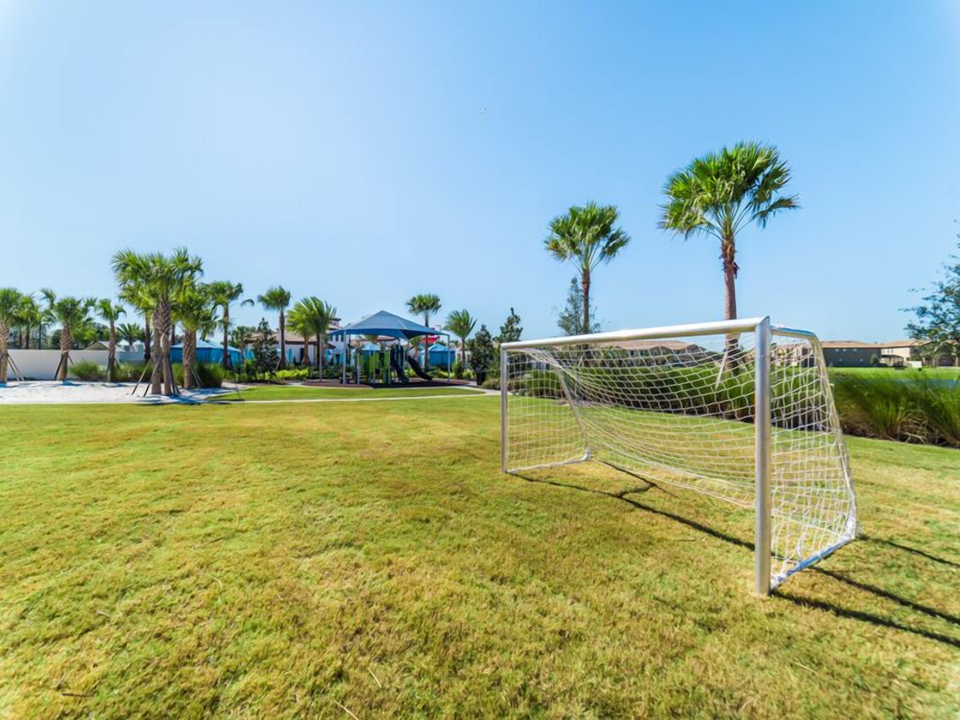 Ein Fußballtor in einer grünen Wiese mit Palmen und einem Pavillon im Hintergrund.