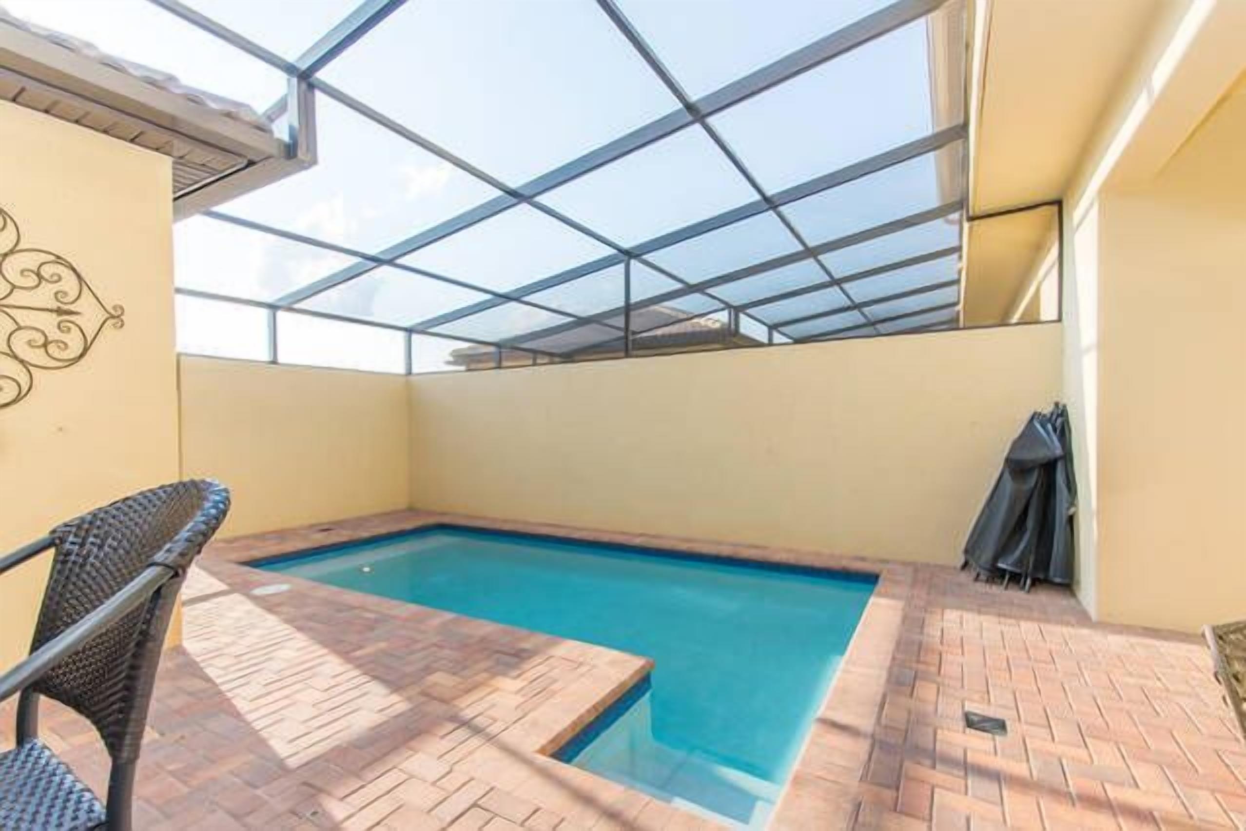 Una piscina con techo de vidrio, rodeada por un patio de ladrillo.