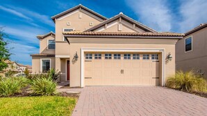 A two-story house with a beige exterior, a garage, and a brick driveway. - Rolling Fairway Home (Davenport)