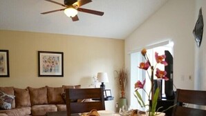 Un coin repas avec une table dressée pour quatre personnes, un ventilateur de plafond et des œuvres d’art encadrées accrochées aux murs.