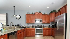 A kitchen with wooden cabinets, stainless steel appliances, a granite countertop, and a tiled floor. - 1408 Wexford Way (Davenport)