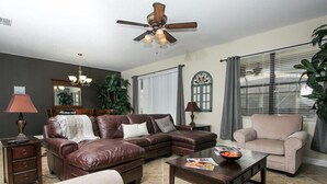 A living room with a brown leather sectional sofa, a beige armchair, a wooden coffee table, and a ceiling fan. - 1408 Wexford Way (Davenport)