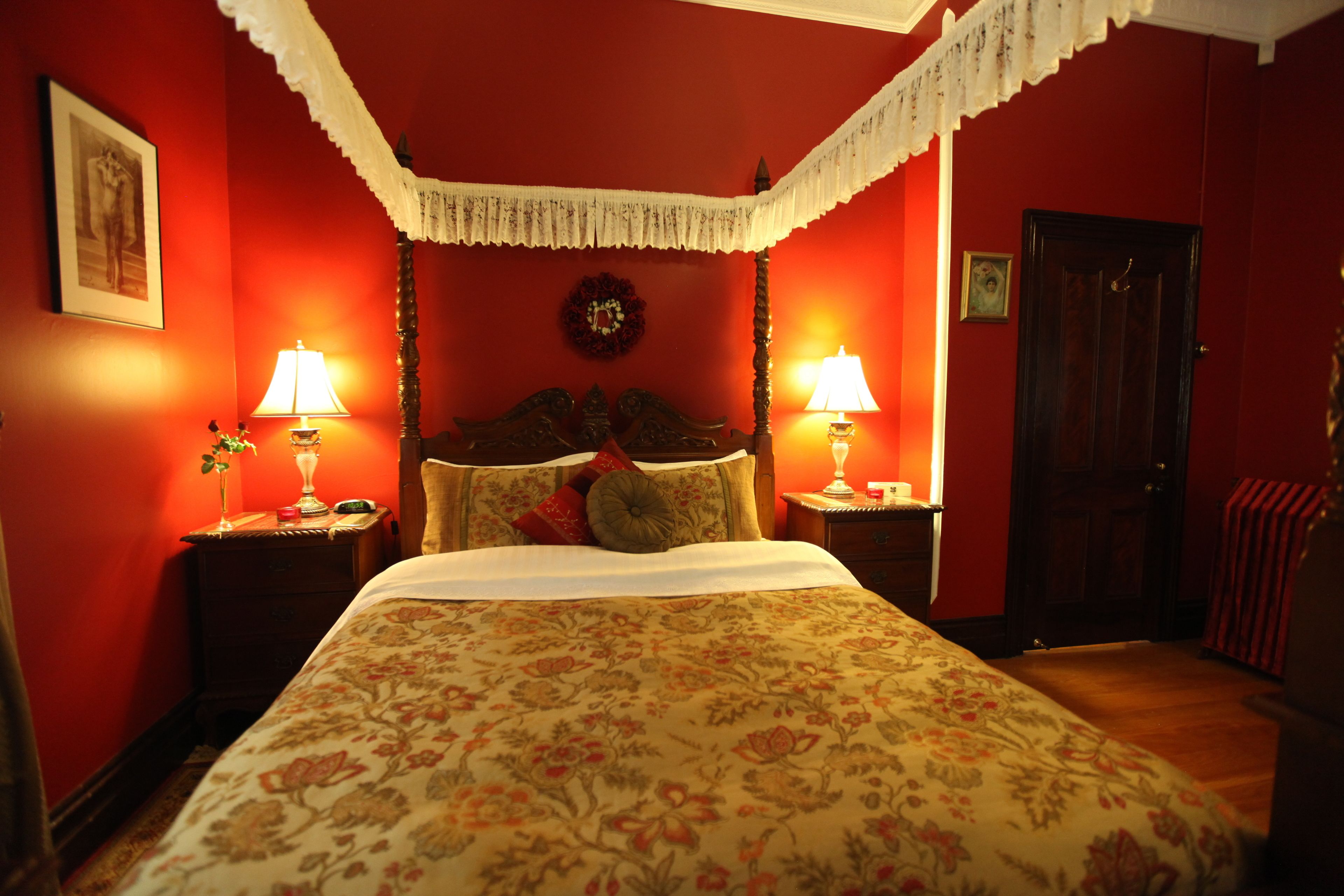 A room with a bed, two bedside tables, a nightstand, a door, and a wall with a framed picture.