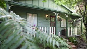 Ein grünes Haus mit Veranda, weißem Zaun und hängenden Blumenkörben.