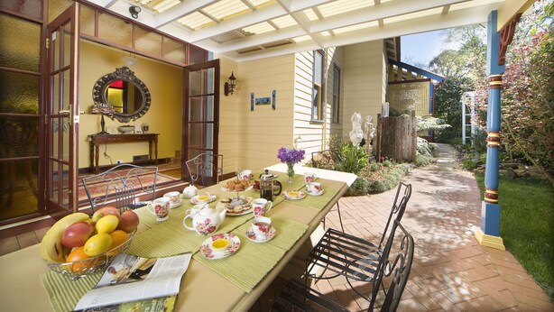 Eine überdachte Terrasse mit Esstisch, gedeckt für das Frühstück, mit verschiedenen Früchten und Gebäck.