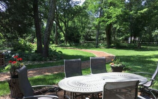 An outdoor patio with a round table and chairs, surrounded by a lush garden and trees. - St Francis Cottage (Chattanooga)