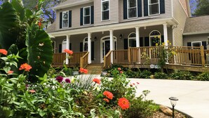 A two-story house with a porch, a front deck, and a garden with various flowers. - St Francis Cottage (Chattanooga)