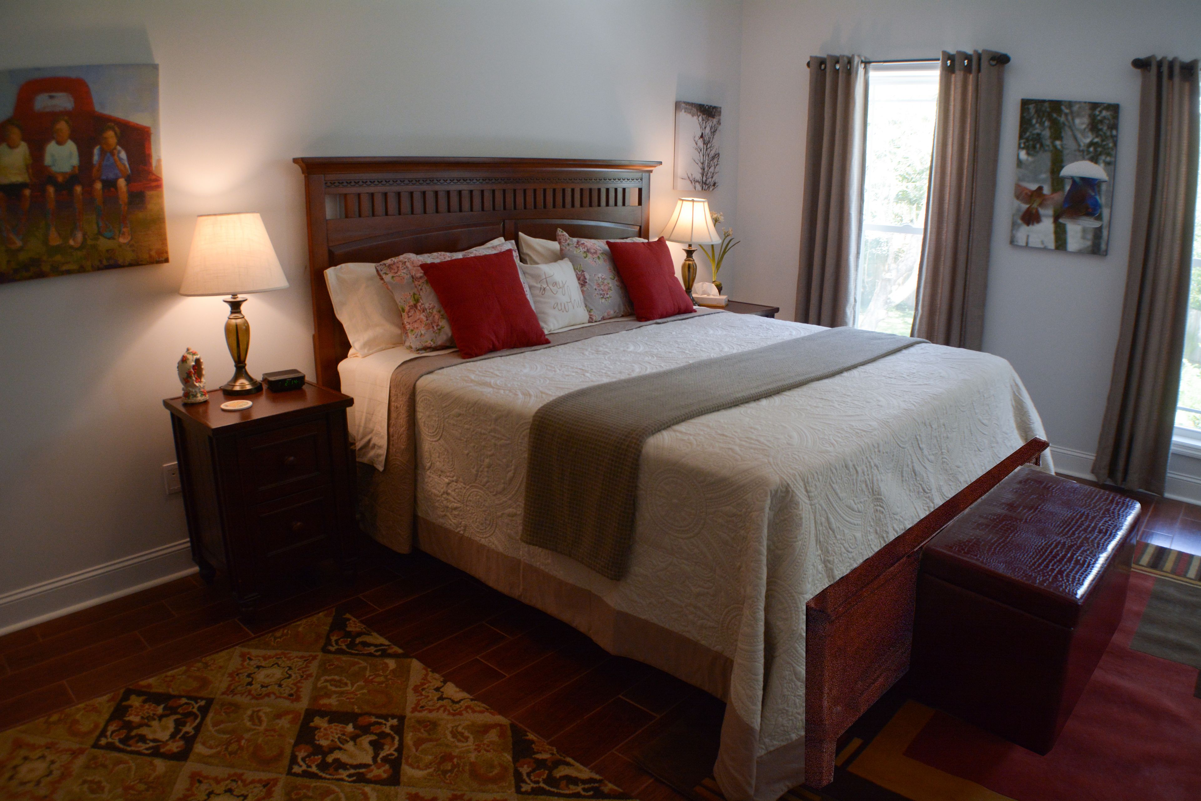 A neatly arranged bedroom with a large bed, a nightstand with a lamp, a small table with a vase, and a decorative rug.