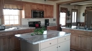 A kitchen with wooden cabinets, a microwave, a stove, a sink, and a window. - Red Cardinal Bed and Breakfast (Carlisle)