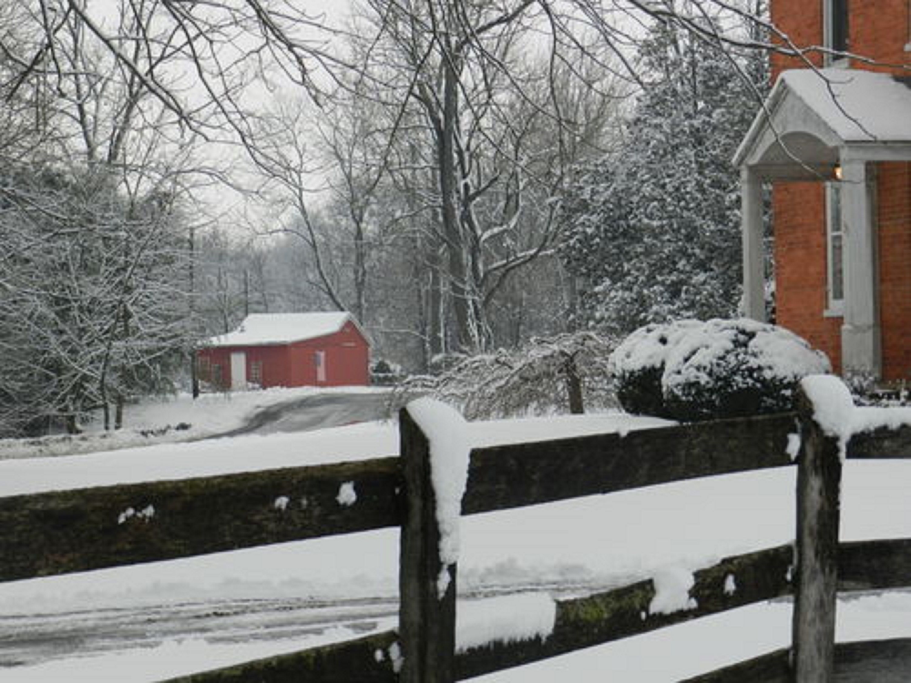 A snow-covered wooden fence with a small red building in the background.