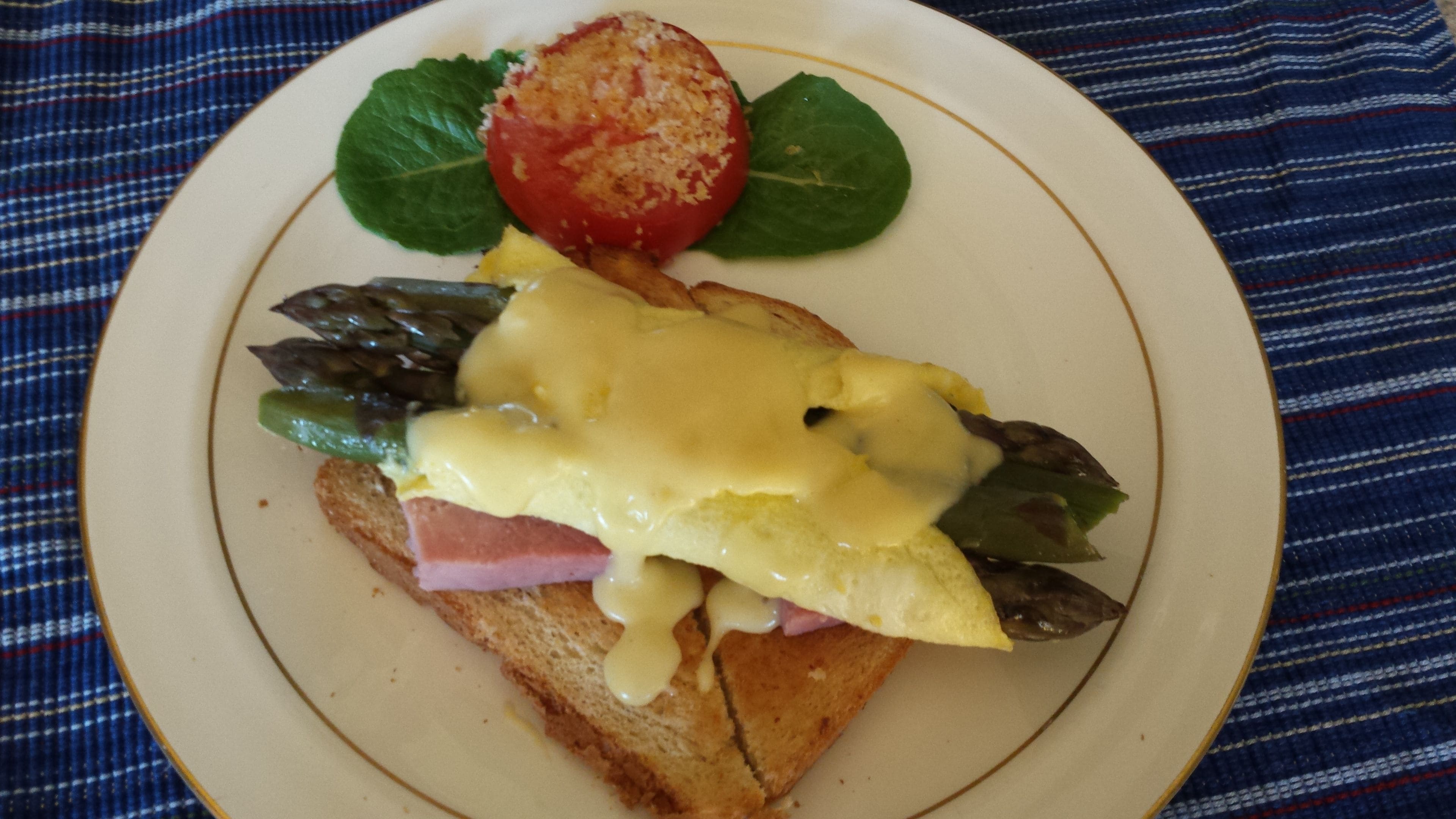 A plate with a sandwich, asparagus, a slice of tomato, and a leaf of spinach.