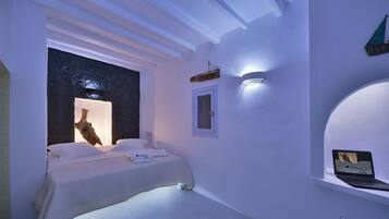 Un dormitorio moderno con cama, una mesita de noche, una computadora portátil sobre una estantería y una lámpara fijada a la pared.