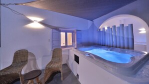 A spa area with a hot tub, wicker chairs, and a covered seating area. - Amo Suites & Spa (Folegandros)