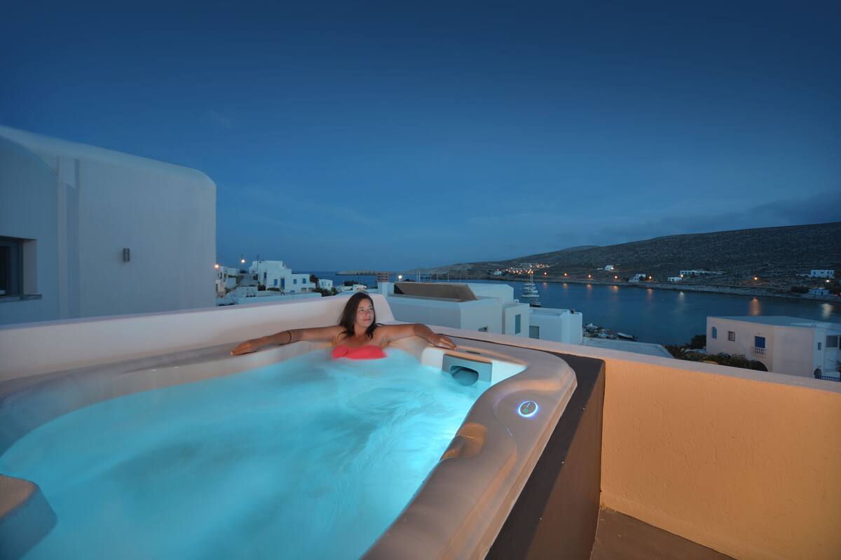A woman relaxing in a hot tub with a view of a harbor and buildings in the background.