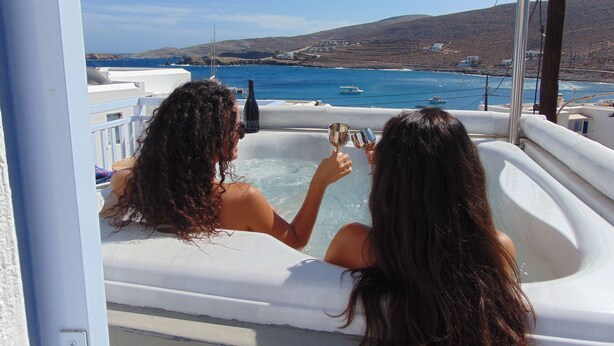 Two people in a hot tub with a view of the sea and hills. - Amo Suites & Spa (Folegandros)