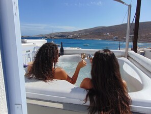 Dos personas en un jacuzzi con vista al mar y colinas.