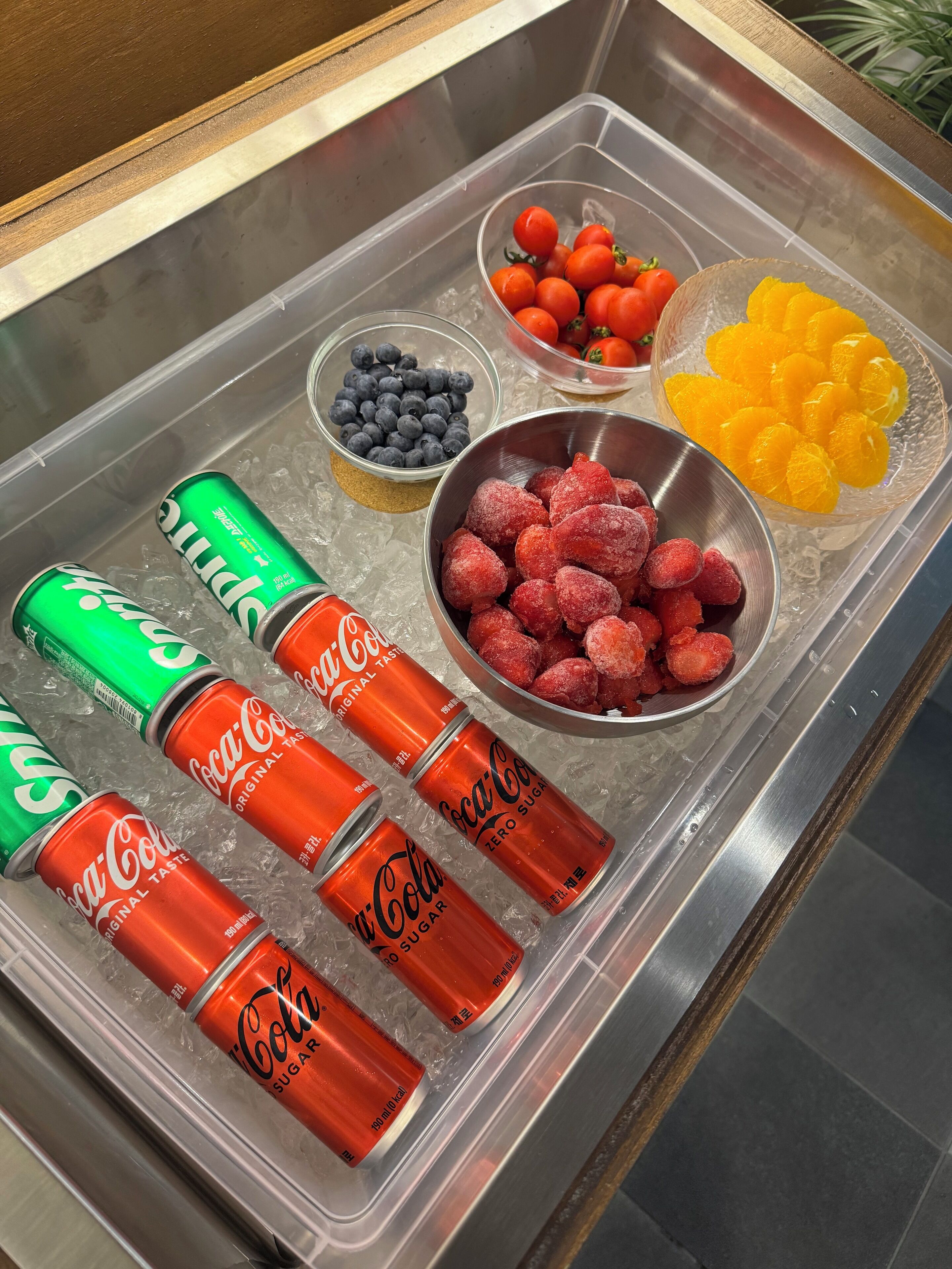 A beverage dispenser with Coca-Cola cans and bowls of blueberries, strawberries, and oranges.