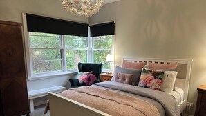 A bedroom with a bed, a chair, a desk, and a window with a view of greenery.