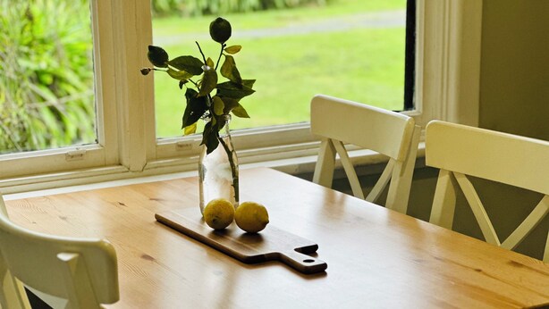 A wooden table with a glass vase containing a plant and two lemons on a cutting board.