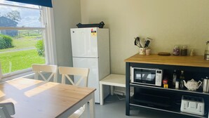 A compact kitchen with a refrigerator, microwave, and toaster. A dining table with chairs is positioned near a window with a view of a green landscape.