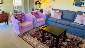 A living room with two pink armchairs, a blue sofa, a black coffee table, and a patterned rug.