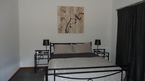 A bedroom with a bed, two bedside tables, a wall-mounted artwork, and a dark curtain.