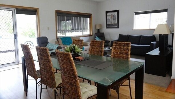 A dining area with a glass table and wicker chairs, a sofa, and a lamp.