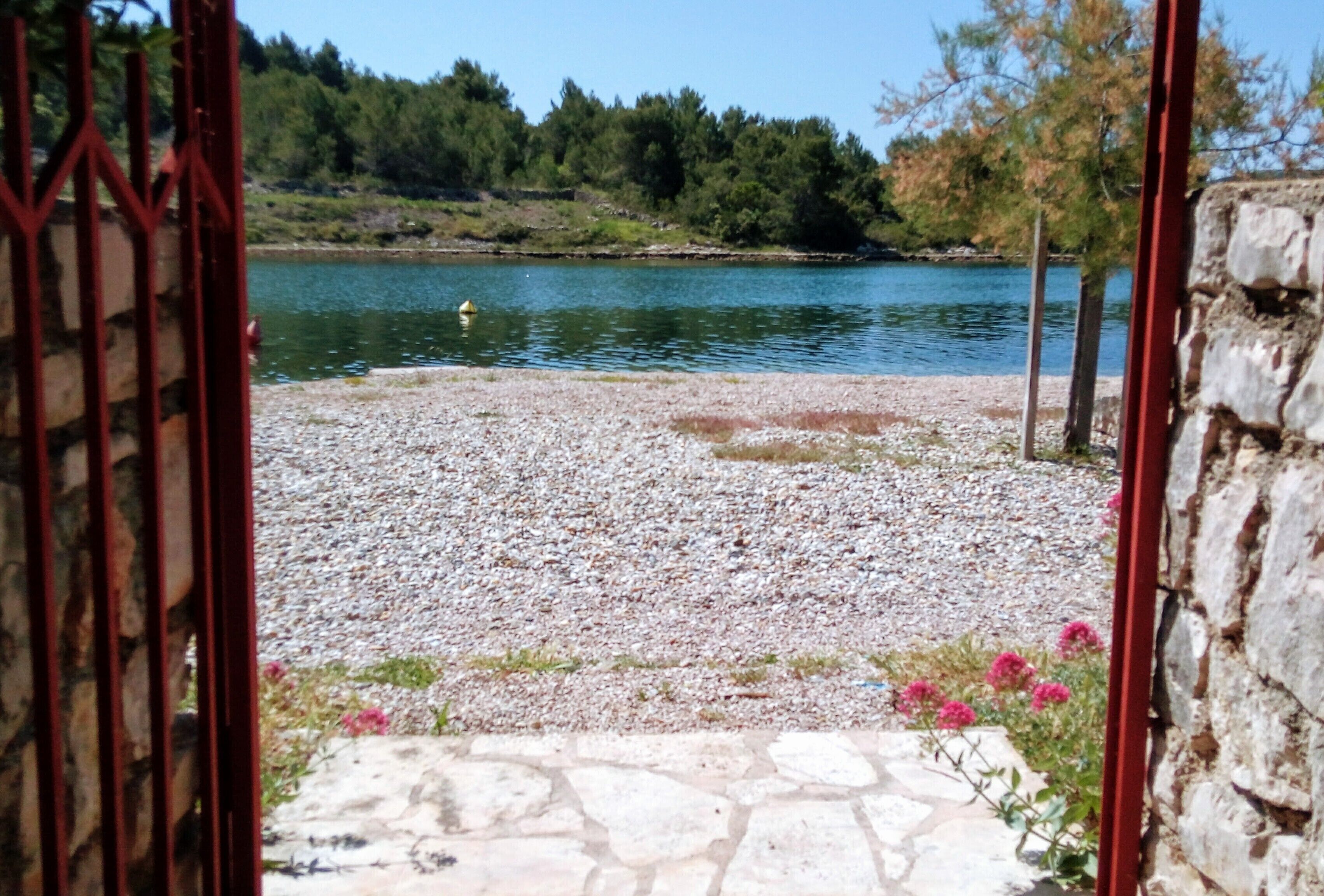 Un sentiero in pietra conduce a una spiaggia di ciottoli, con un corpo d'acqua e alberi sullo sfondo.
