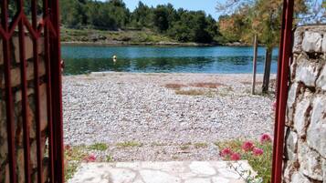 Un sentiero in pietra conduce a una spiaggia di ciottoli, con un corpo d'acqua e alberi sullo sfondo.