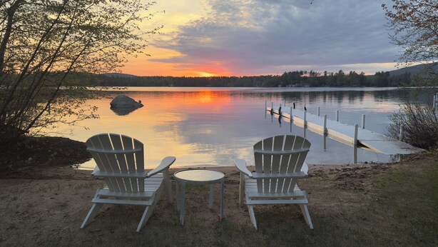 Two Adirondack chairs facing a calm lake with a dock extending into the water. - Sandy waterfront, grass yard, 40' private dock. Foliage week special-Book now! (Moultonborough)